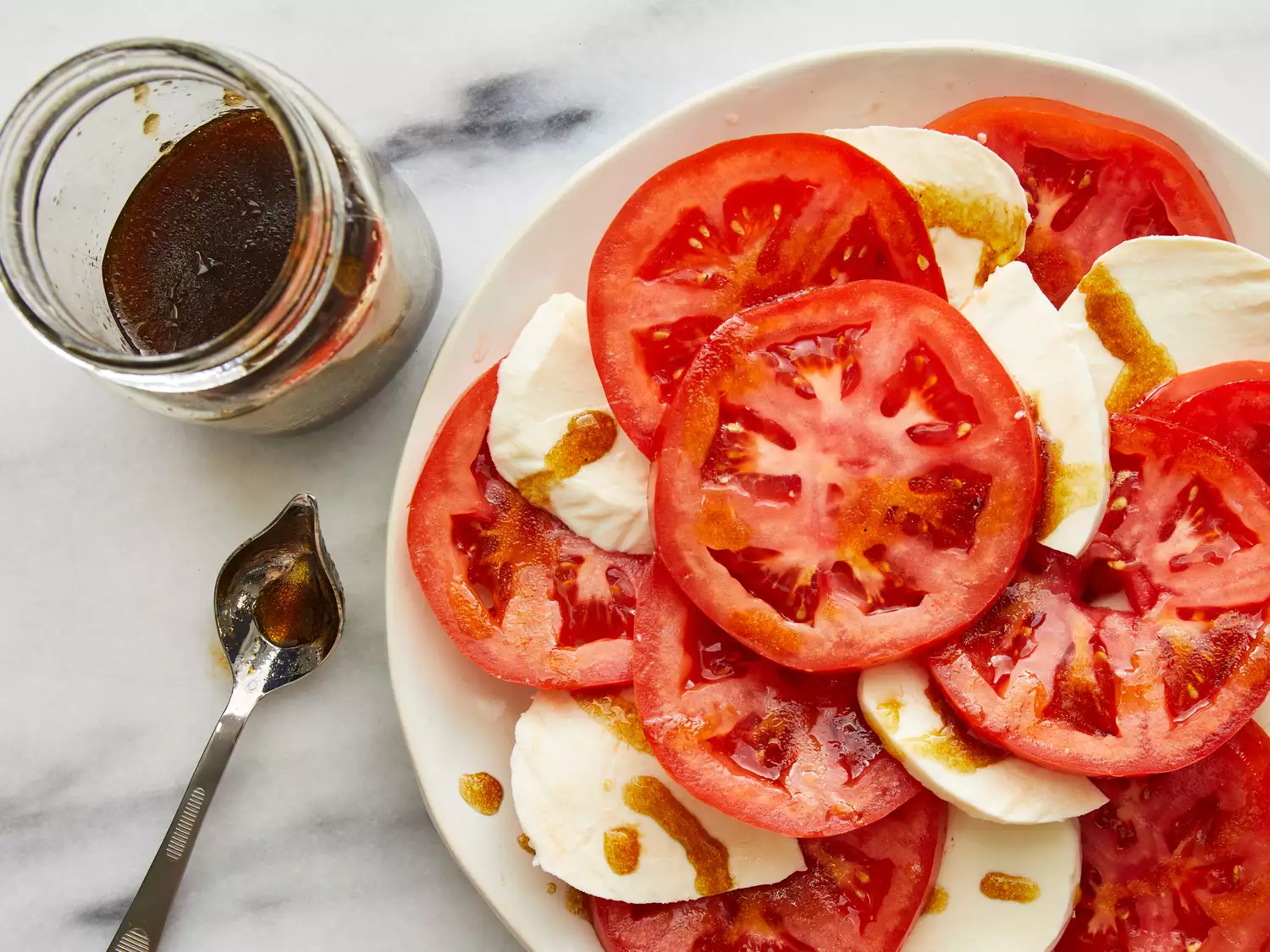Balsamic and olive oil dressing being drizzled evenly over tomato and mozzarella slices