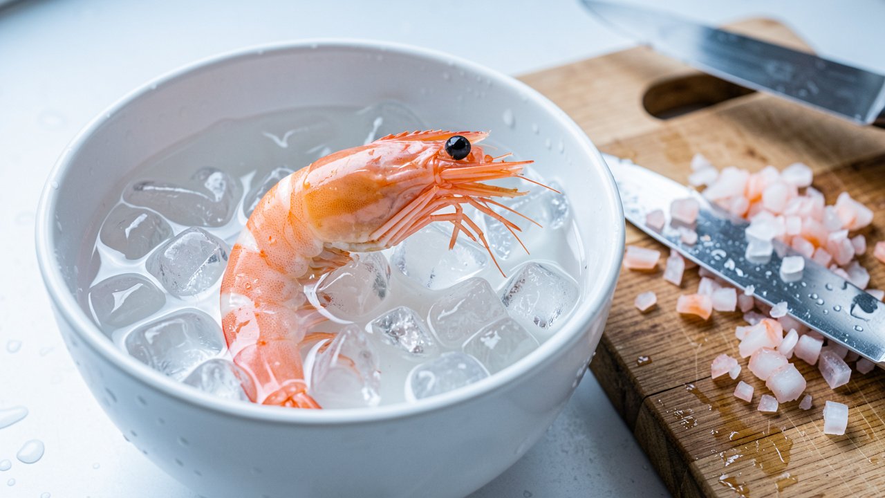 Poached shrimp cooling in ice water beside finely chopped shrimp on a board