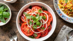 A bright bowl of Tajik shakarob salad with sliced tomatoes, sweet onion, and fresh herbs beside a plate of plov